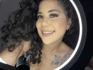 Mulher de cabelos cacheados usando maquiagem glamourosa com delineador e cílios.