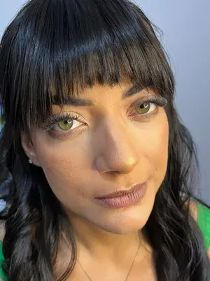 Mulher de franja usando maquiagem natural com olhos verdes em destaque.